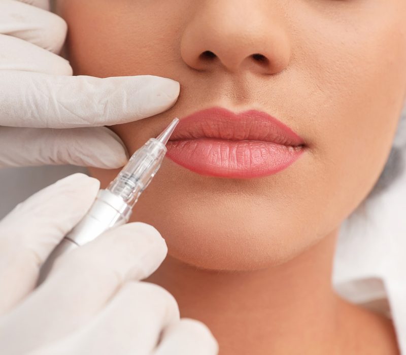 Young woman undergoing procedure of permanent lip makeup in tattoo salon, closeup